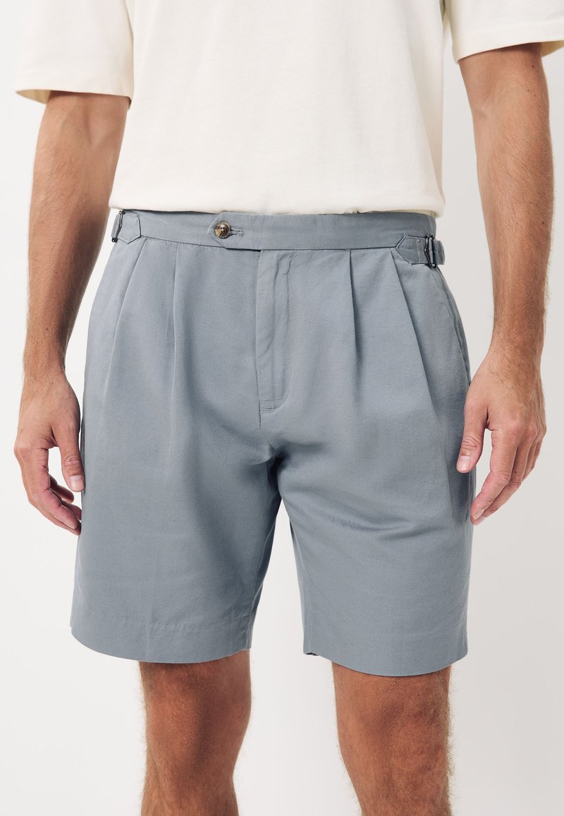 Pantaloncini grigi realizzati in tessuto morbido, caratterizzati da un design plissettato, chiusura con bottoni e cinturini laterali regolabili per una vestibilità su misura.