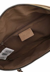 Inredning av tan-handväska med en slät brun foder, en zippered ficka och en läderetikett med präglat varumärke på sidan.