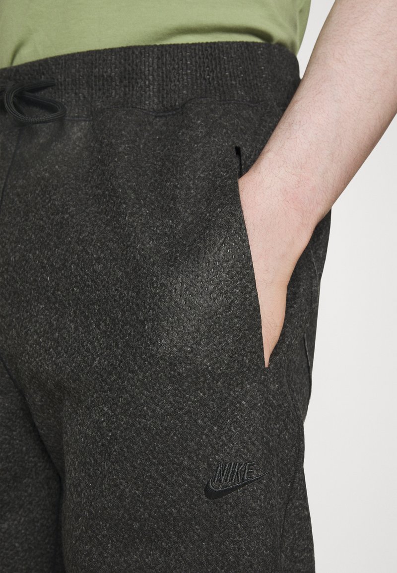 Pantalons de survêtement gris foncé avec une surface texturée, une taille élastique, des poches latérales et un petit logo Nike noir sur le côté gauche.