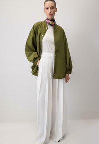 Oliwkowa kurtka o luźnym kroju, ze złotymi napami i balonowymi rękawami, w zestawieniu z białymi spodniami z wysokim stanem i plisowaniem.