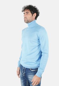 Maglione a collo alto di colore azzurro realizzato in materiale morbido. Caratterizzato da maniche lunghe e collo a coste, abbinato a jeans blu strappati.
