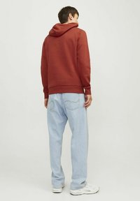 Rød hættejakke med snøre og kængurulomme, parret med lyseblå løse jeans. Hvite sneakers synlige forneden.