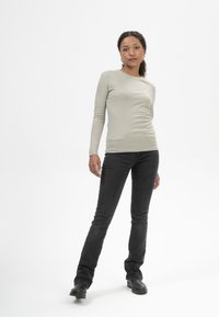 Helles graues Langarmshirt mit rundem Halsausschnitt und taillierter Passform, kombiniert mit schwarzen Slim-Fit-Jeans und schwarzen Stiefeletten.