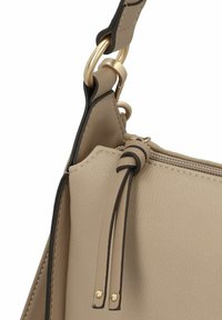 Beige leren handtas met een gestructureerde afwerking, voorzien van gouden hardware en contrasterende donkere details. Inclusief rits en decoratieve franjes.