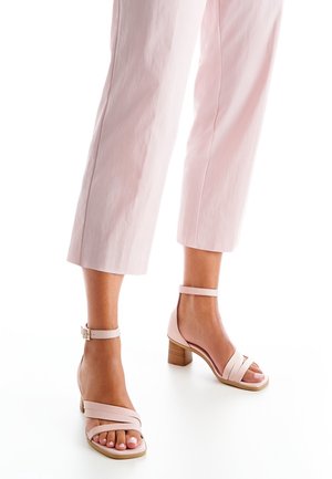 Rosa Leder-Pumps mit Knöchelriemen, offenem Zehenbereich und überkreuztem Design. Ausgestattet mit einem hellen Holz-Blockabsatz und glatter Textur.