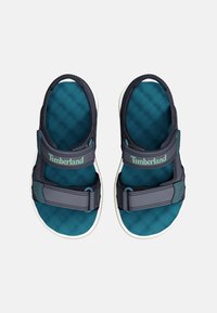 Sandali blu scuro e teal con cinturini regolabili, soletta strutturata e suole bianche. Presentano il marchio Timberland sui cinturini.