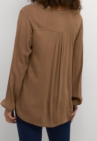 Bruine blouse met lange mouwen, ontspannen pasvorm, textuur-stof en plooien op de schouders. De zoomlijn is gebogen met een gladde halslijn.