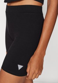 Sorte ribbete sykler med en glatt midjebånd og en liten trekantet logoak accent nær kanten. Stoffet ser ut til å være elastisk og tettsittende.