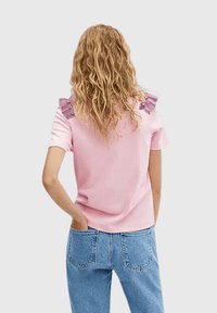 Camiseta rosa con detalles de volantes en los hombros en color púrpura claro con adornos azules; corte holgado y mangas cortas.