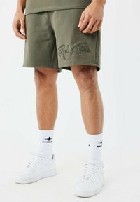 Shorts en coton vert olive avec logo brodé "Project x Paris", offrant une coupe décontractée. Associés à des baskets blanches et des chaussettes.