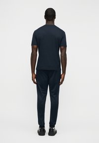 Σκούρο μπλε κοντομάνικο μπλουζάκι συνδυασμένο με τζόγκερς με στενή γραμμή στο τελείωμα. Το ύφασμα φαίνεται απαλό και λείο· τα τζόγκερς έχουν ελαστικές μανσέτες και πλευρικά ραφή.