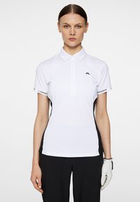 Vit pikétröja med krage, korta ärmar, svarta sidopaneler och en liten logga på bröstet. Bärs med svarta byxor och en handske.