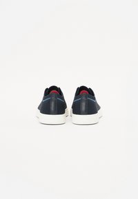 Sneakers blu navy con tomaia in mesh testurizzato, suole in gomma bianca e dettagli rossi sul tallone. Design elegante e minimalista.