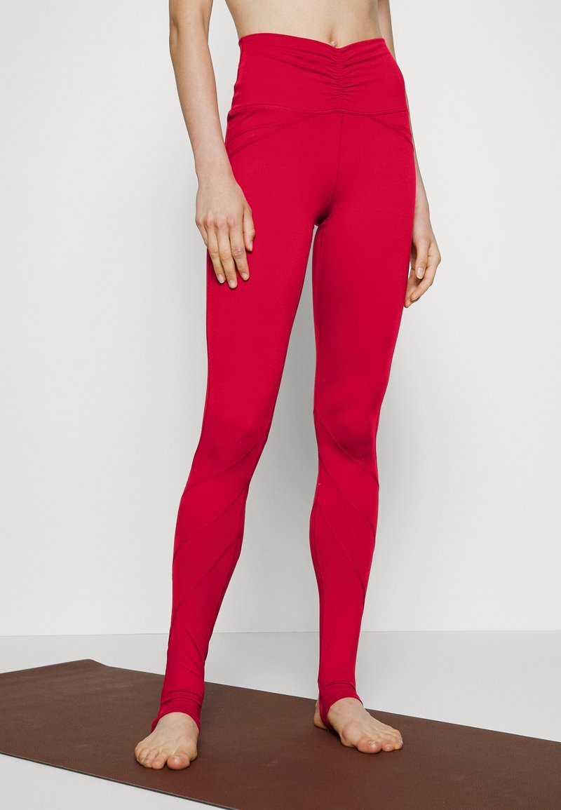 Vysoké červené legíny vyrobené z elastického materiálu, s nařaseným designem v pase a diagonálními švy.