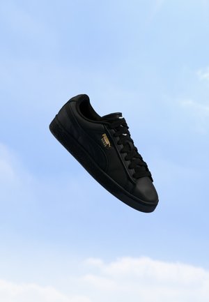 Черна маратонка Puma от велур с черни връзки, плаваща на фона на ясно синьо небе.