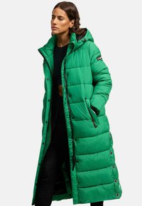 Parka verte longue et gonflée avec capuche, dotée de accents de fermeture éclair noirs, de boutons-pression et d'un motif matelassé.