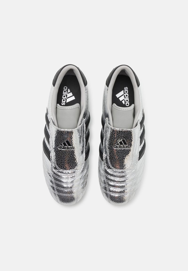 Botas de fútbol sintéticas plateadas con una superficie texturizada, rayas negras y una lengüeta y un interior acolchados en gris. Logotipo de Adidas visible.