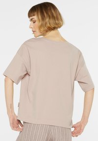 Hellrosa übergroßes T-Shirt mit kurzen Ärmeln, gerundetem Ausschnitt und Seitenetikett-Detail. Hergestellt aus weichem Baumwollstoff mit glatter Textur.