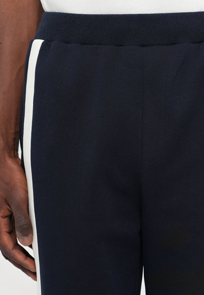 Navy jogger pants made from a soft fabric feature a textured waistband and white side stripes, showcasing a clean design with a relaxed fit.