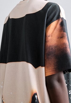 T-shirt featuring a blend of black, beige, and brown hues with a distinct pattern. Made of soft fabric with a relaxed fit and short sleeves.