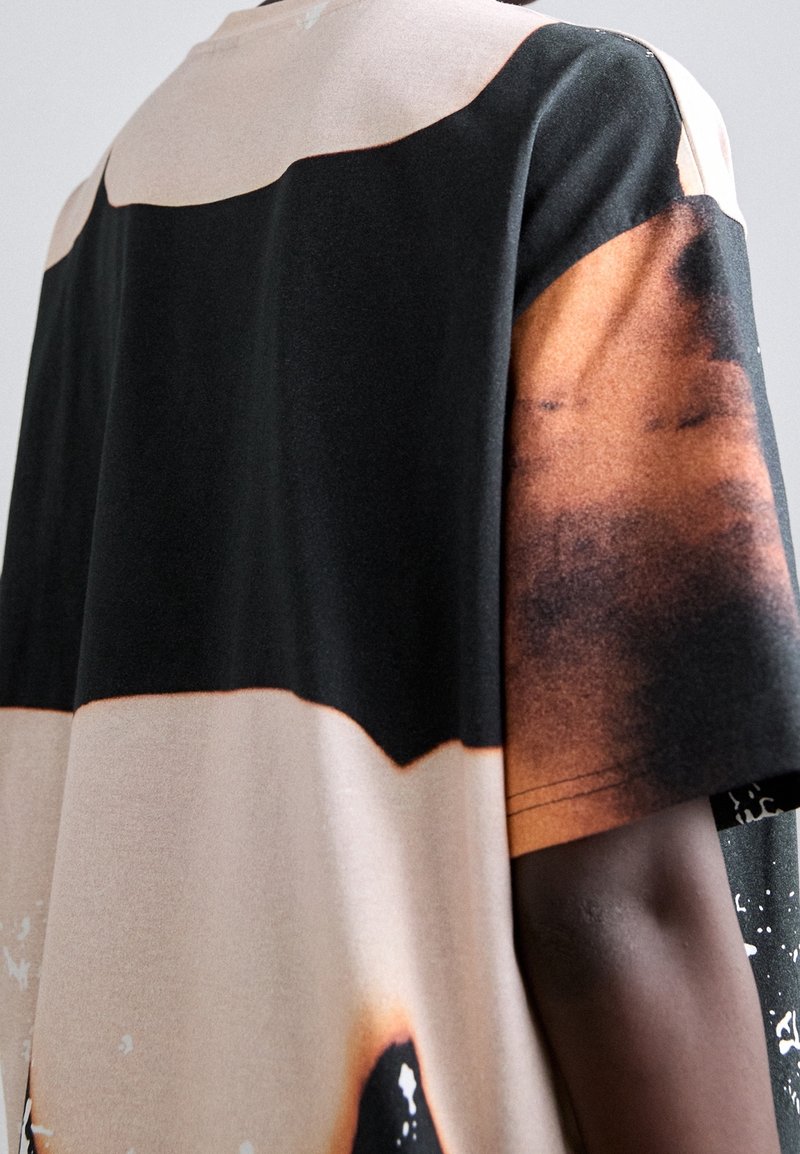 T-shirt présentant un mélange de nuances noires, beiges et brunes avec un motif distinct. Confectionné en tissu doux avec une coupe décontractée et des manches courtes.