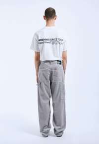 Witte katoenen T-shirt met zwarte tekst en grafiek op de achterkant, gecombineerd met grijze corduroy cargo-broek met zijzakken en een textuurstof.