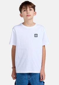 Witte katoenen t-shirt met een ronde hals, korte mouwen en een marineblauw logo op de linkerborst. Draag het met blauwe denim shorts.