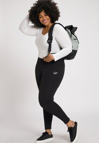 Zwarte leggings met UP-logo, witte longsleeve top en zwarte sneakers. De rugzak is zwart en lichtgrijs met verstelbare bandjes.