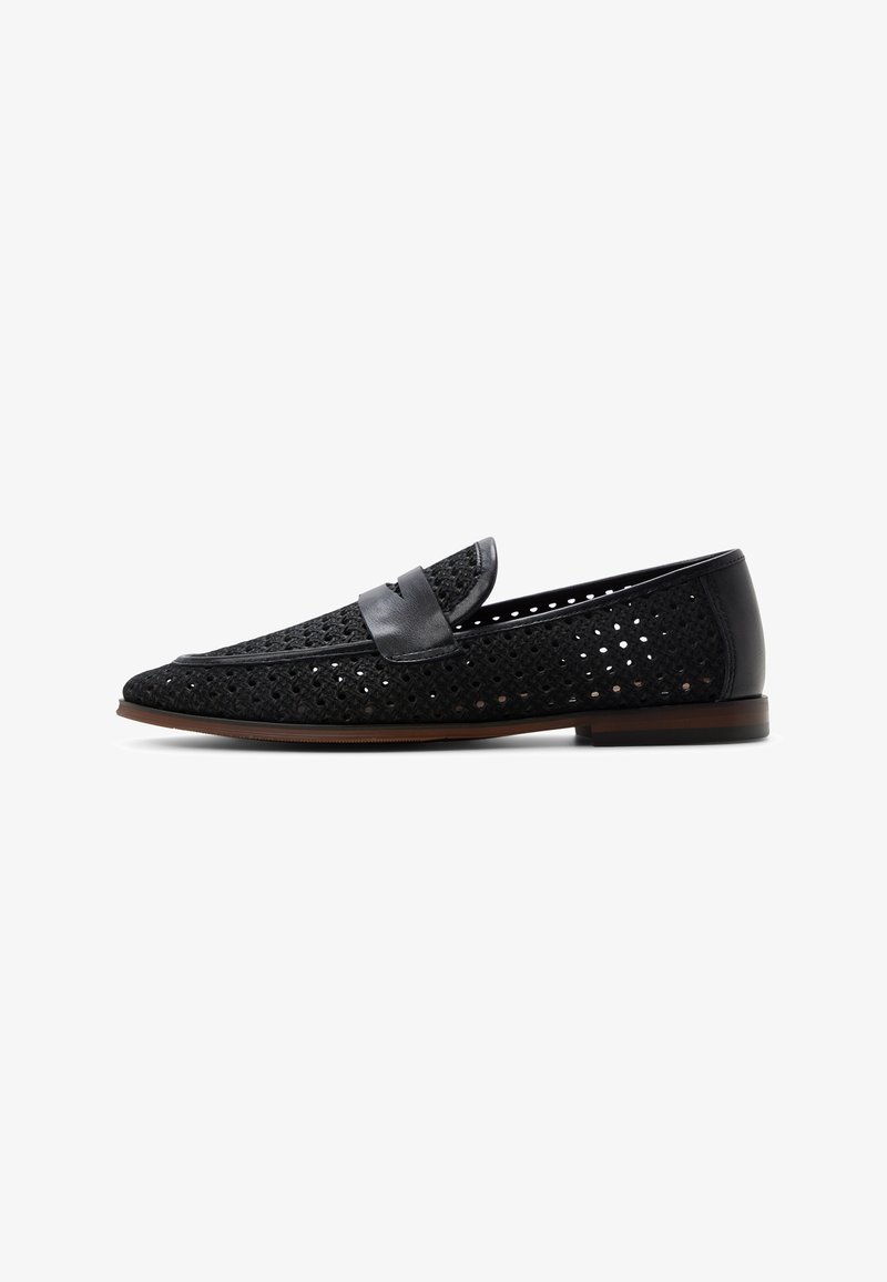 Mocasín de cuero negro perforado con correa tipo penny y suela marrón, mostrado de perfil sobre fondo blanco.