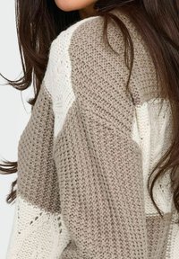 Maglione lavorato a maglia con un design a blocchi di colore beige e bianco e motivi testurizzati. Il tessuto appare morbido e spesso, aumentando il calore.