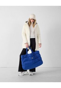 Sac fourre-tout bleu matelassé avec texture rembourrée, grande taille et deux poignées. Le tissu semble léger et a un éclat.