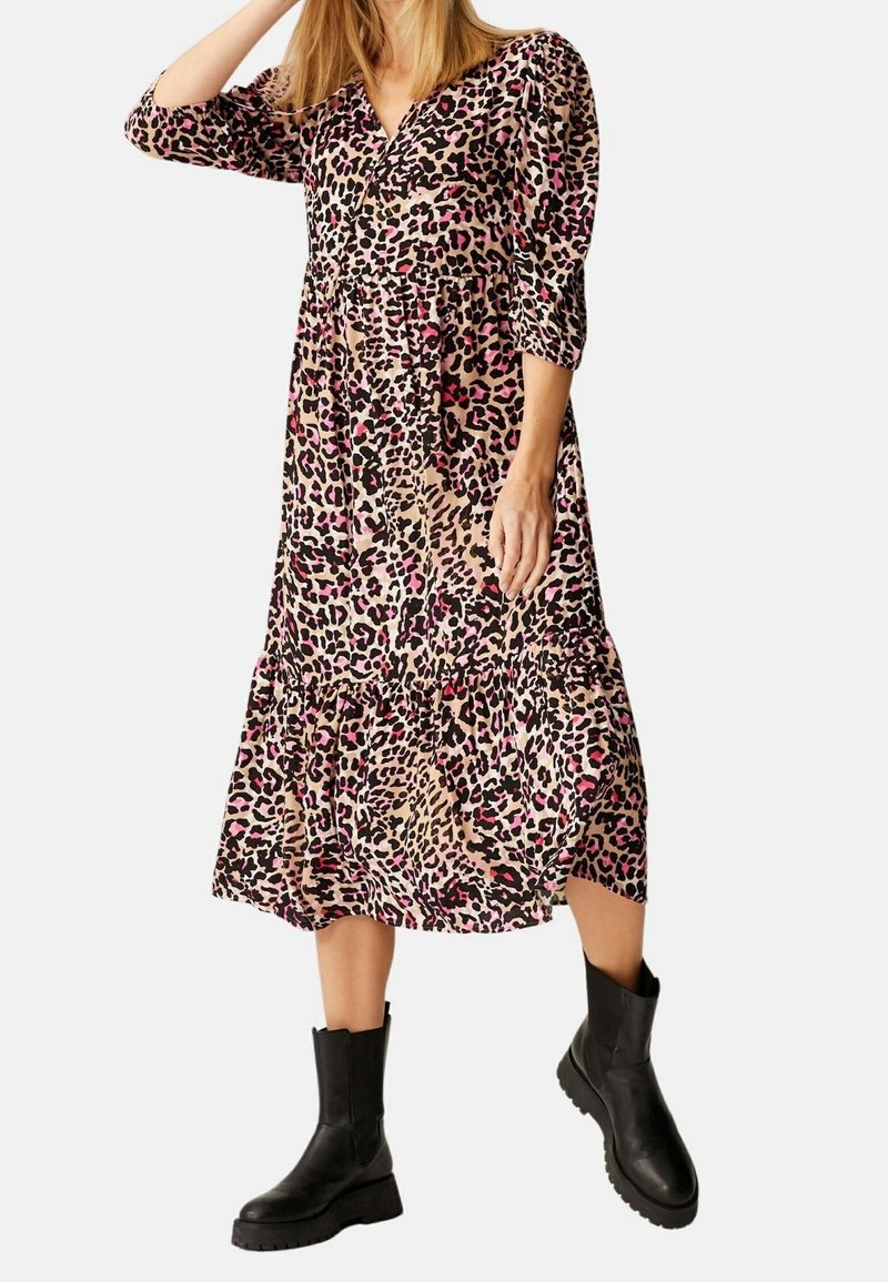 Femme portant une robe mi-longue à imprimé léopard avec des accents roses et des bottines noires, avec des manches trois-quarts et un col en V.