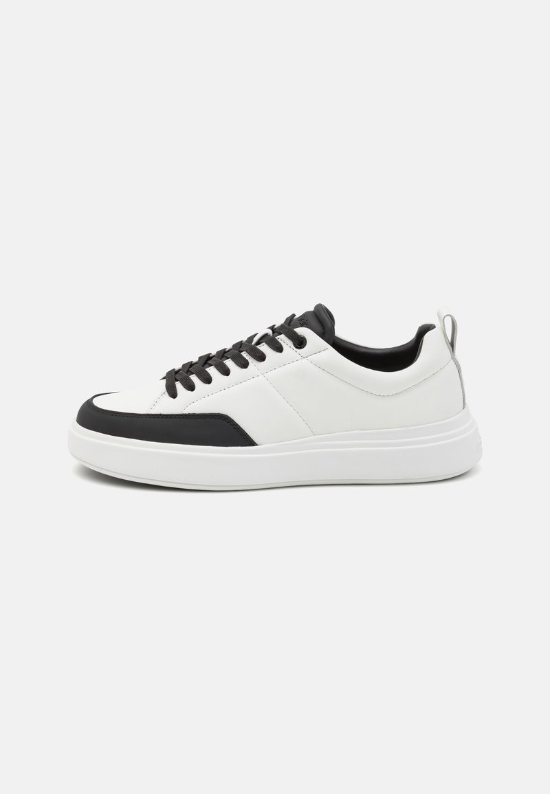 Baskets en cuir avec un corps blanc, des accents noirs, un bout arrondi et des lacets noirs. Comprend une épaisse semelle blanche et une tirette à l'arrière.