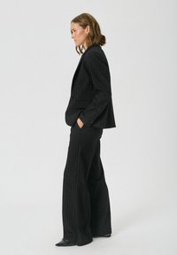 Blazer noir à rayures et ensemble de pantalons à jambes larges. Tissu lisse avec un éclat subtil. Le blazer présente des revers classiques et des poches latérales.