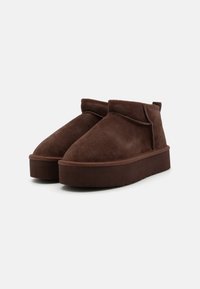 Stivaletti in suede marrone con punta arrotondata e suola piatta, caratterizzati da un design cucito e una linguetta sul retro.