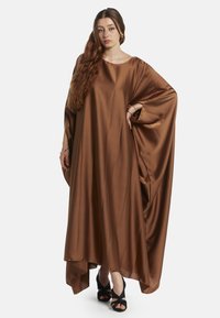 Abito kaftano in satin marrone con collo rotondo, maniche ampie e orlo irregolare, abbinato a scarpe con tacco alto nere.