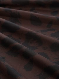 Bruine stof met zwart abstract luipaardprintpatroon, getoond met zachte plooien die zachte schaduwen en textuur creëren.