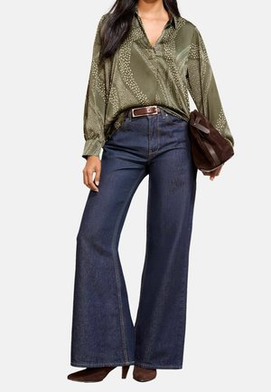 Kvinde iført mørkeblå vidde jeans, olivengrøn mønstret bluse, brun bælte, brune hælede sko og bærer en brun ruskindstaske.
