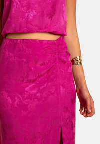 Ensemble fuchsia en deux pièces comprenant un haut sans manches et une jupe taille haute avec une texture florale, une fente sur le côté et des détails froncés sur la jupe.