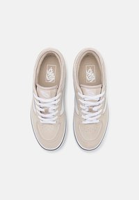 Beige suede sneakers with white laces and textured accents. Features a padded collar and logo on the tongue, with a black rubber sole.