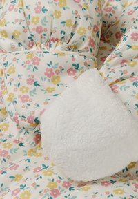 Blumengemusteter Stoff mit pinken, gelben und blauen Blumen auf cremefarbenem Hintergrund, mit einem weichen weißen Fleece-Akzent und gerafften Nähten.