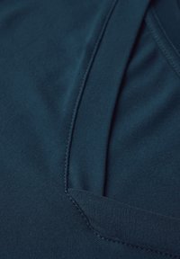 Ciemnoniebieski top z tkaniny o gładkiej strukturze, z okrągłym dekoltem i wyszywanymi detalami na brzegach. Prosty, minimalistyczny design.