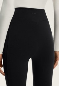 Zwarte high-waisted legging gemaakt van gladde rekbare stof, met een logo op de achterste tailleband en een getailleerde pasvorm.
