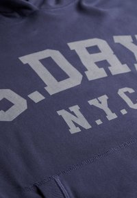 Sudadera de algodón azul marino con gran texto gris "O.D.A.Y N.Y.C." en el pecho, tela texturizada y un bolsillo tipo canguro.