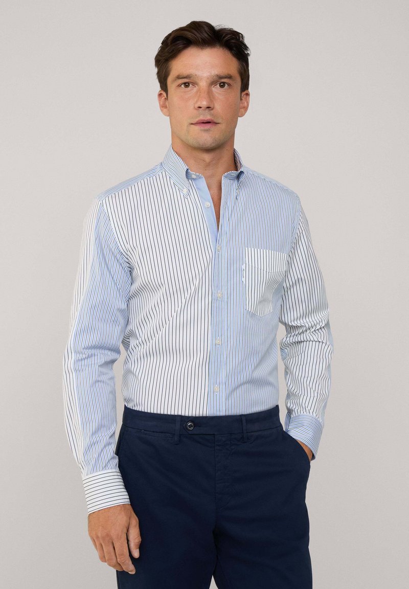 Camisa de botones a rayas en blanco y azul, con un bolsillo en el lado izquierdo, combinada con pantalones azul marino. Tejido de algodón suave, corte ajustado.