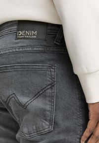 Džíny z tmavě šedého denimu s texturovaným povrchem. Mají zadní kapsu se cikcak stehem a značenou koženou nášivku s nápisem "DENIM TOM TAILOR".