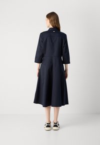 Donkerblauwe jurk met driekwartmouwen en een uitlopende rok. Katoenen stof met een gematigde glans. De achterkant heeft een kraag en een logo-details.