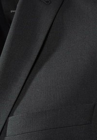 Veste de costume noire en tissu texturé, avec des revers aigus et une poche poitrine unique, mettant en avant un design formel.