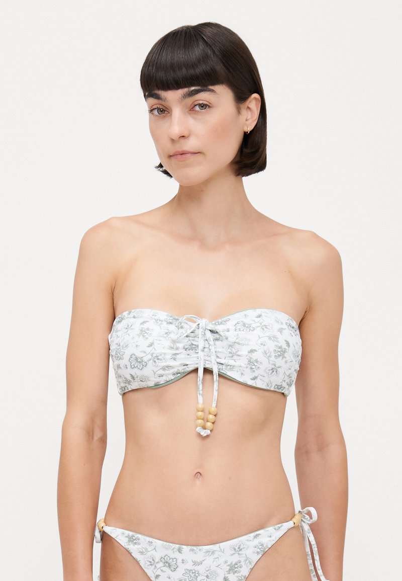 Bikini set s cvjetnim uzorkom u bijeloj i zelenoj boji, bandeau gornji dio sa završecima za zatezanje i perlicama; donji dio s bočnim vezicama i detaljima od perlica.