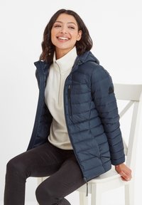 Navy puffer jacket with a hood, zippered front, and quilted texture. Worn over a cream fleece top, features side zipper pockets.